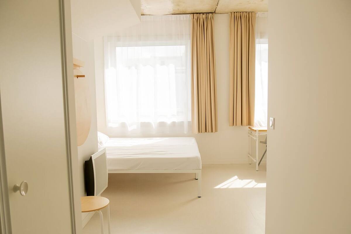 A minimalist bedroom with a single bed, a small table, and a chair.