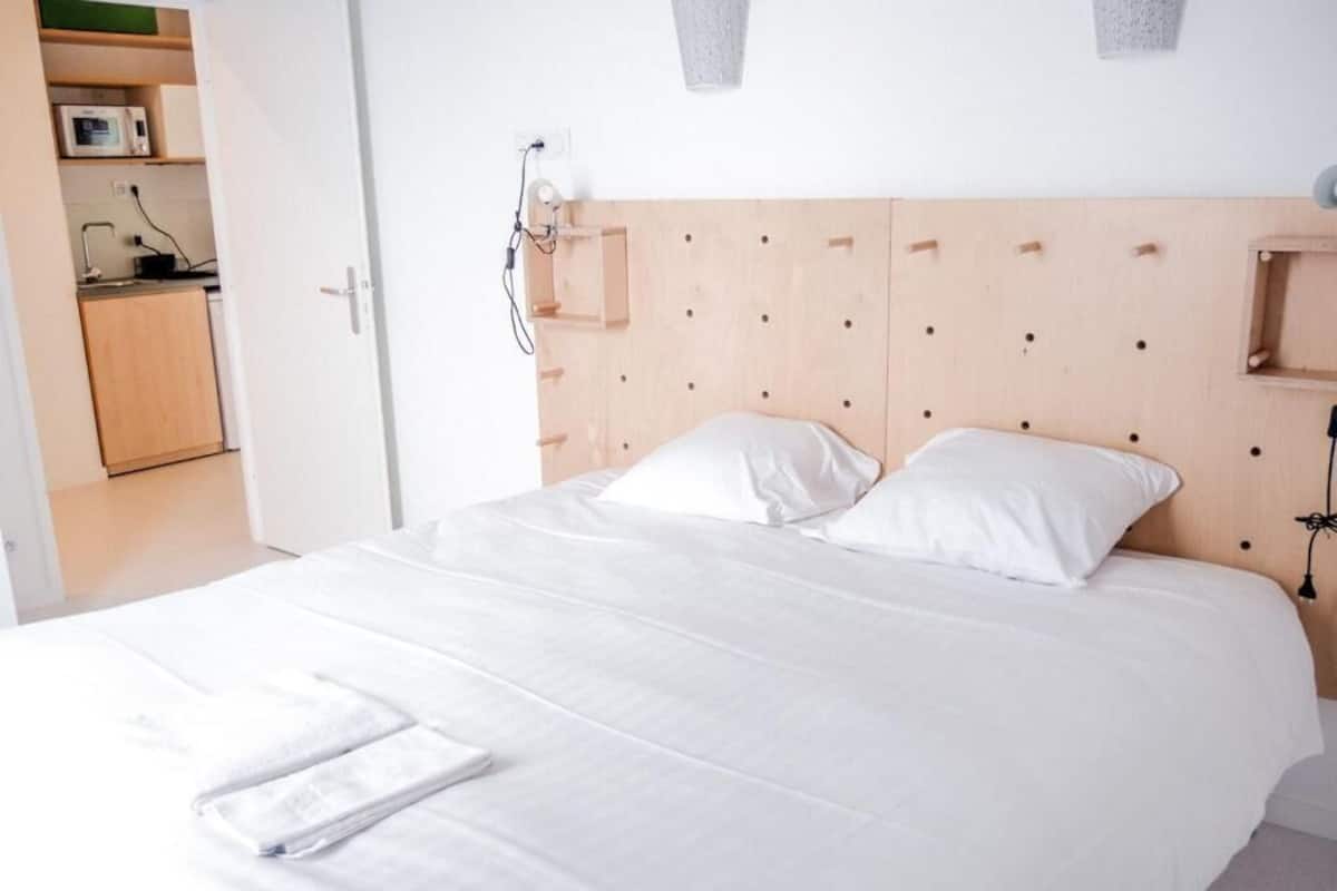 A neatly made bed with white linens and pillows, a wooden headboard, and a small bedside table with a lamp.