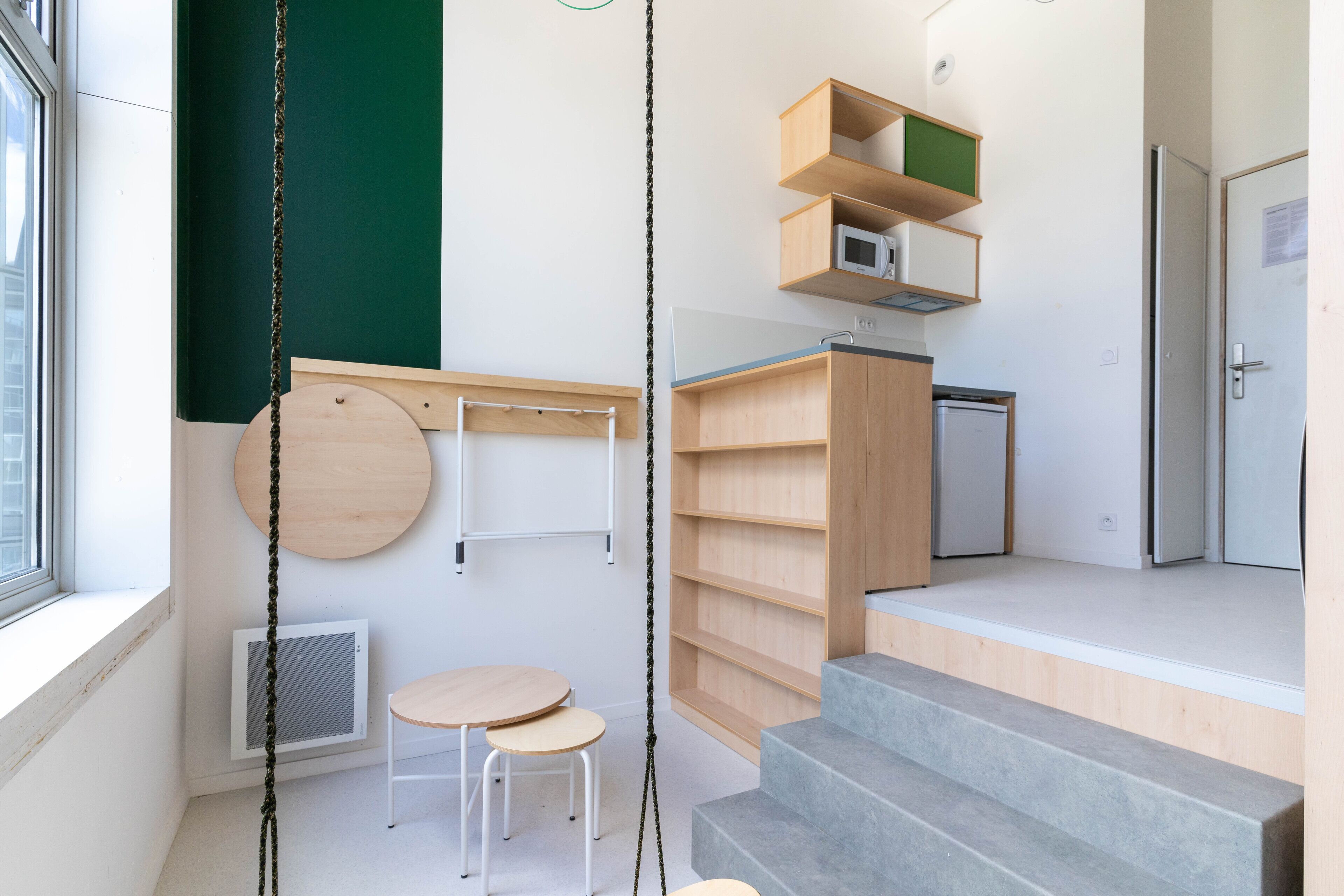 A modern interior with a staircase, wooden shelves, a small table, and a hanging chair.