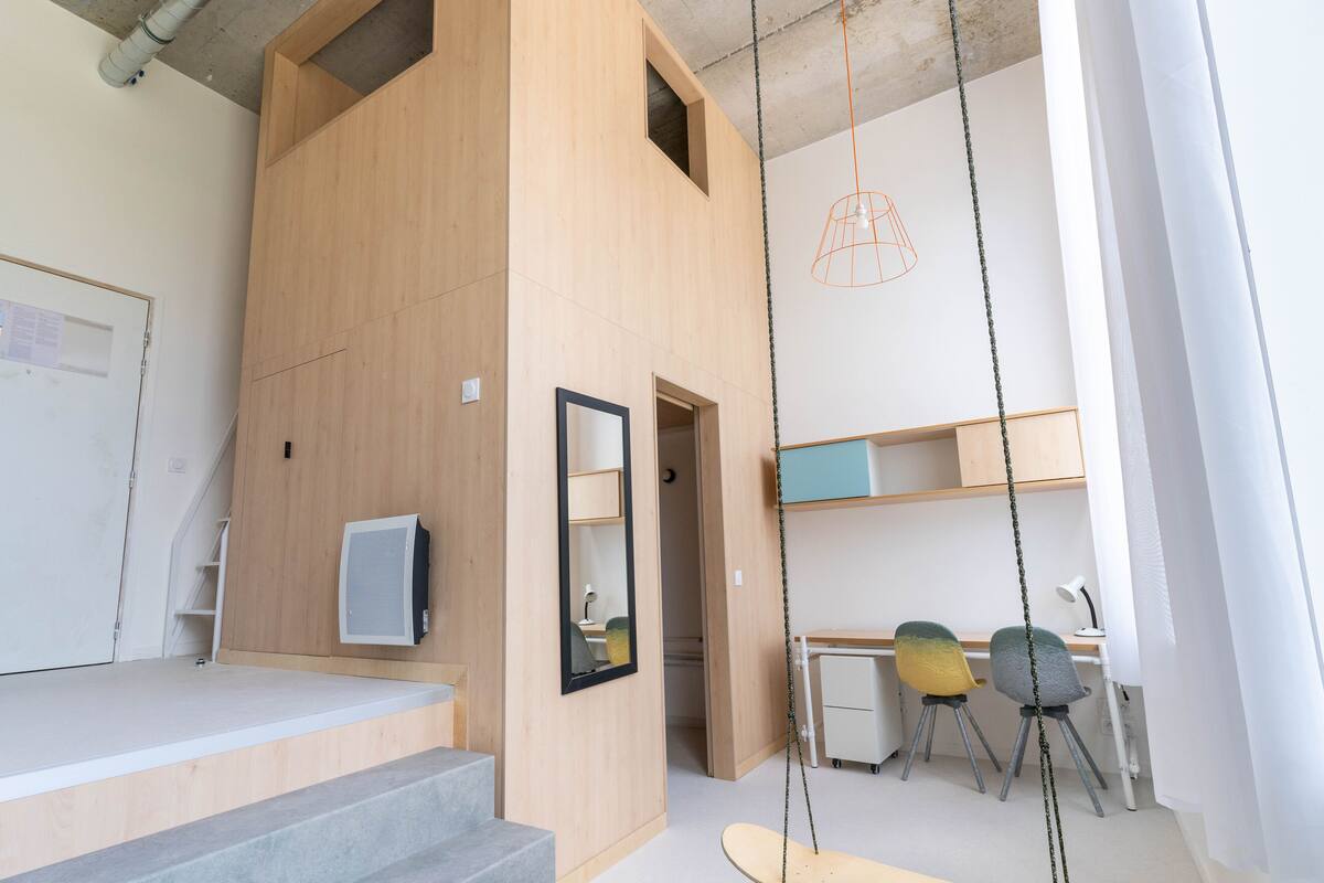 A modern room with a wooden accent wall, a desk with two chairs, a hanging light fixture, and a television.