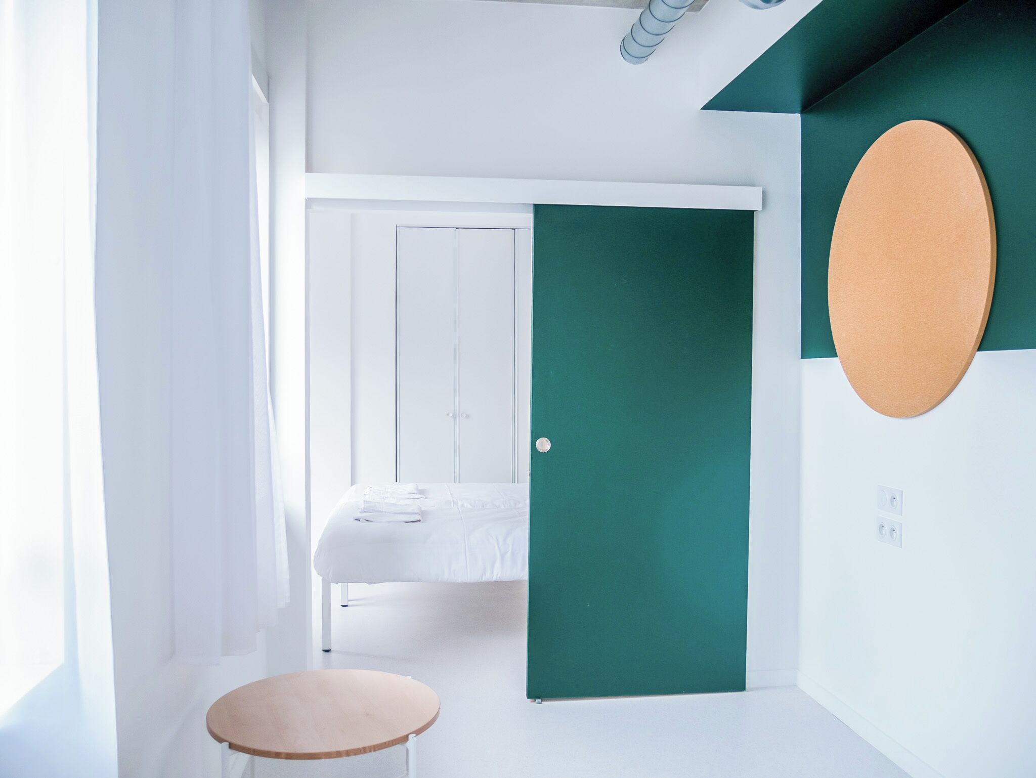 Une pièce minimaliste avec un lit, une petite table ronde et une porte verte.