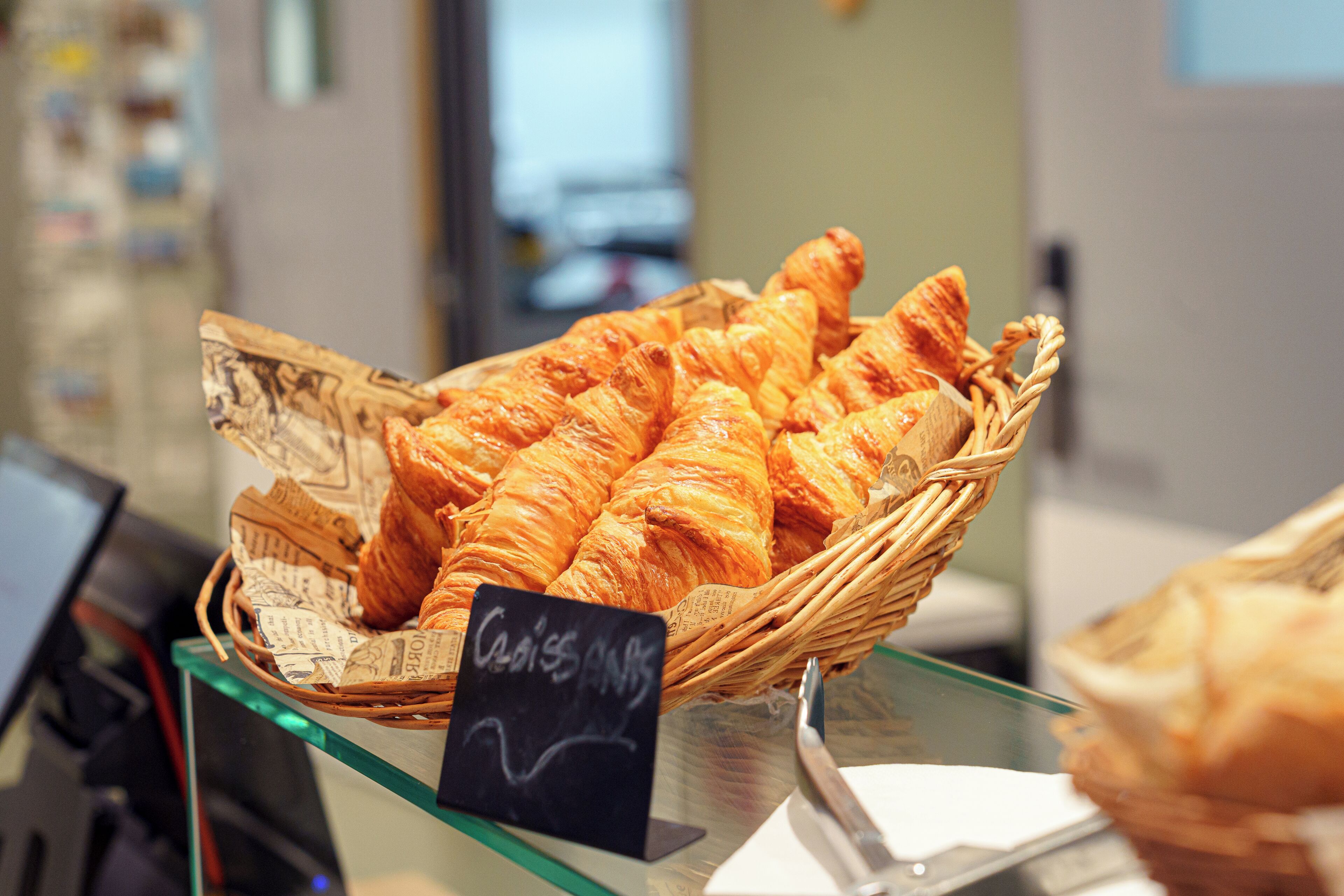 Una cesta de cruasanes sobre un expositor de vidrio con un letrero que dice 'Croissants'.