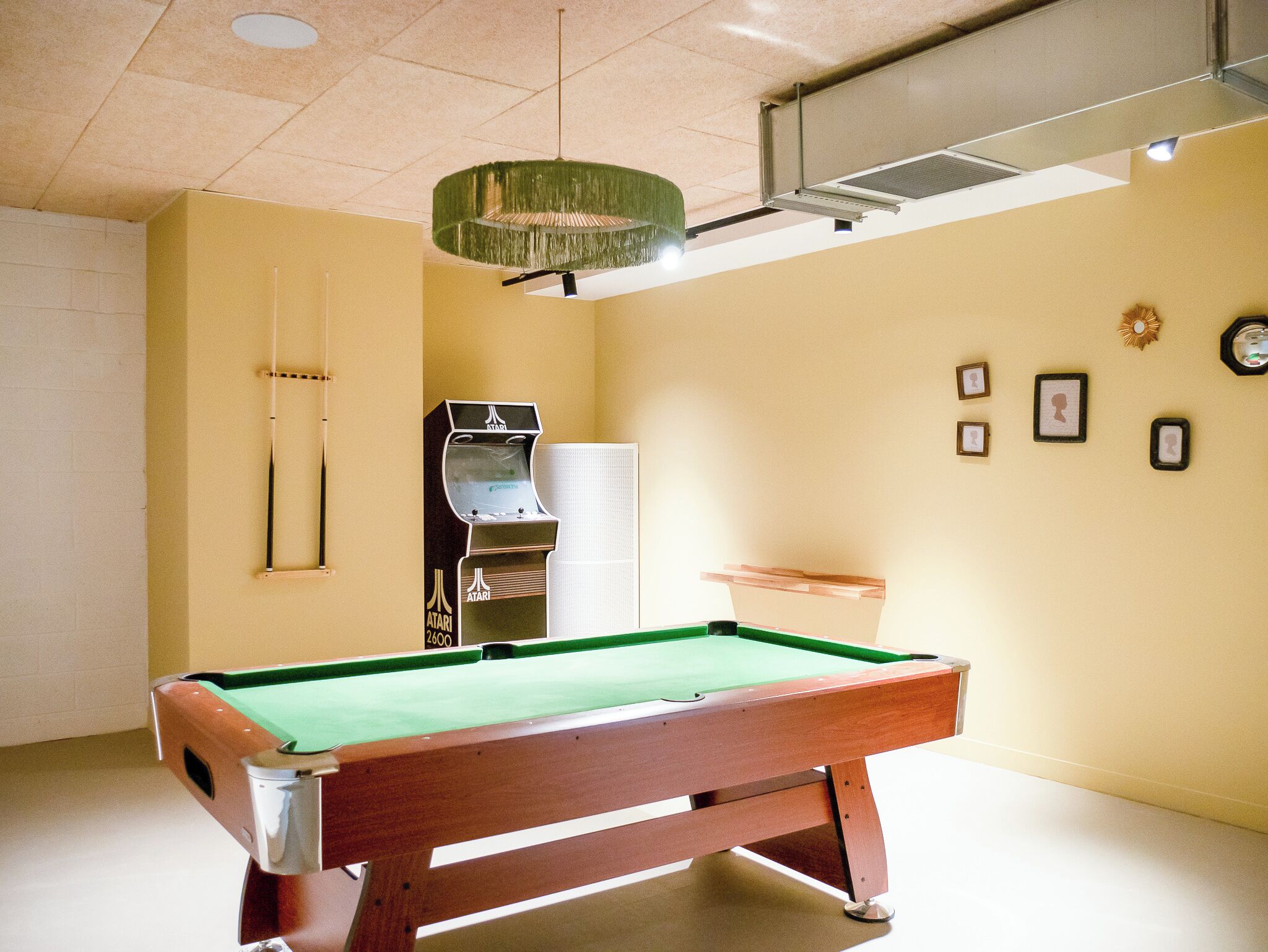 Ein Billardtisch in einem Raum mit Deckenventilator, gerahmten Bildern an der Wand und einer Lüftungsanlage.