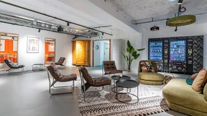 Un área de estar moderna con sillones de cuero, un sofá y una mesita de centro. Se observa una planta grande y una pantalla mural con varios objetos.