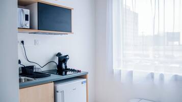 A modern kitchen with a coffee maker, a small refrigerator, and a window with sheer curtains.