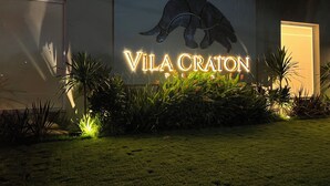 Schild für 'Vila Craton' mit einer Schildkröte, umgeben von gepflegter Bepflanzung und beleuchtet durch künstliche Beleuchtung.
