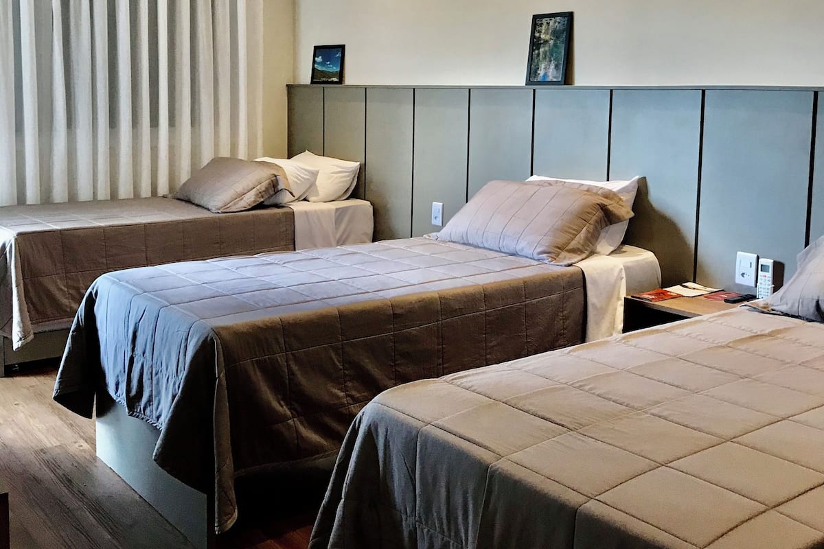 A hotel room with two beds, a headboard, a bedside table, a nightstand, a window with curtains, and a wall-mounted artwork.