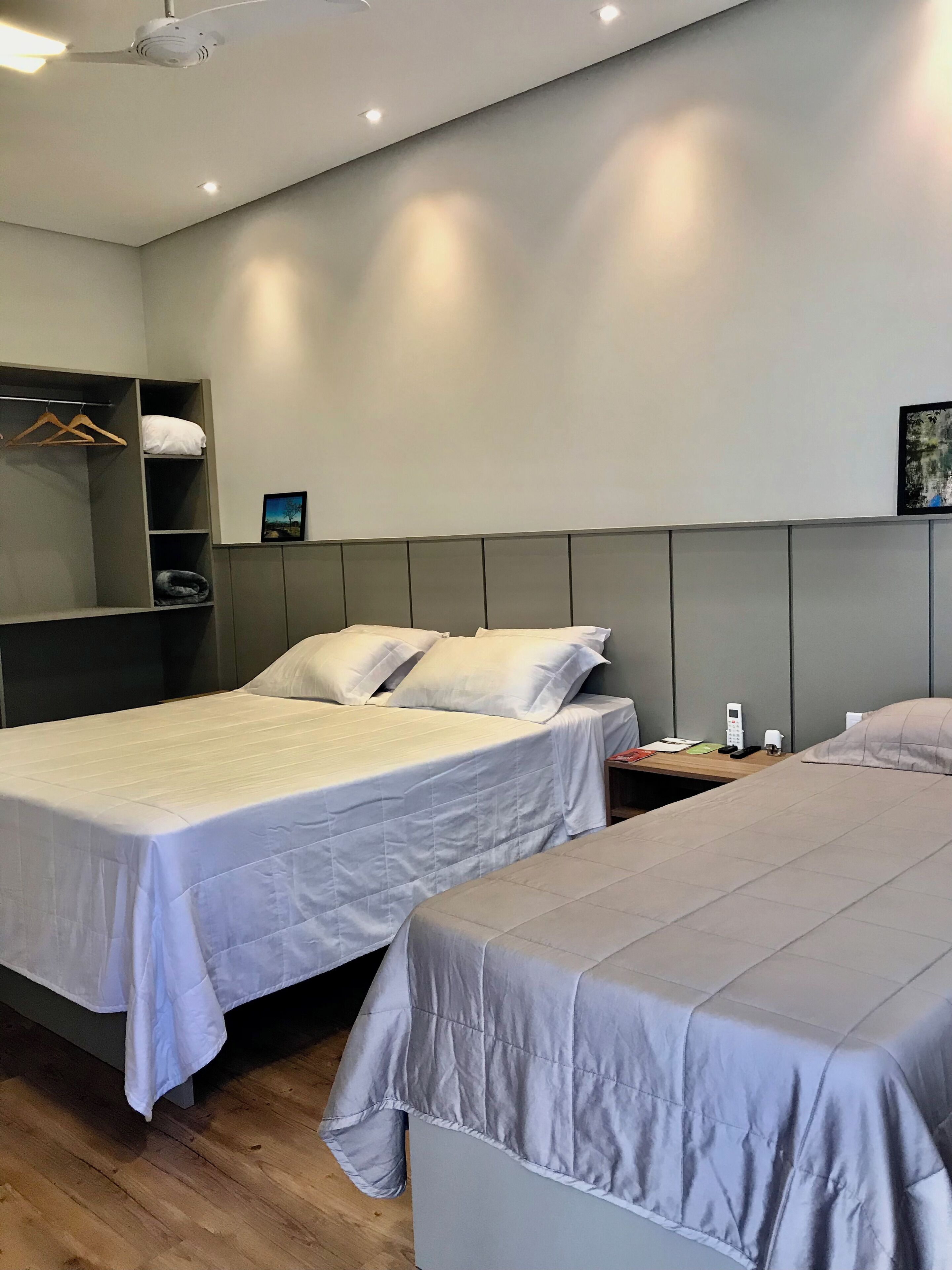 A hotel room with two beds, a wardrobe, a bedside table with a phone, and a painting on the wall.