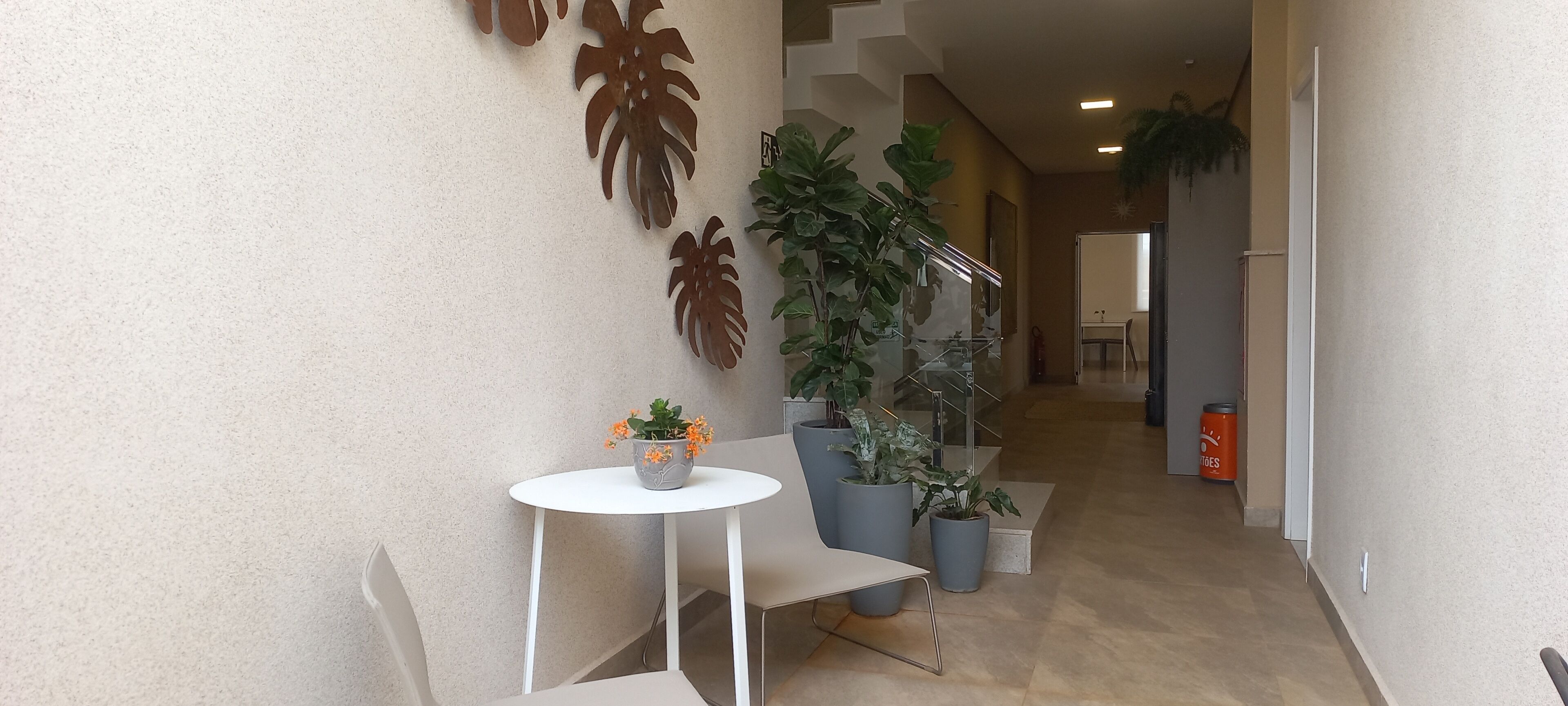 A modern interior with a white table and chairs, potted plants, and a staircase leading to another room.