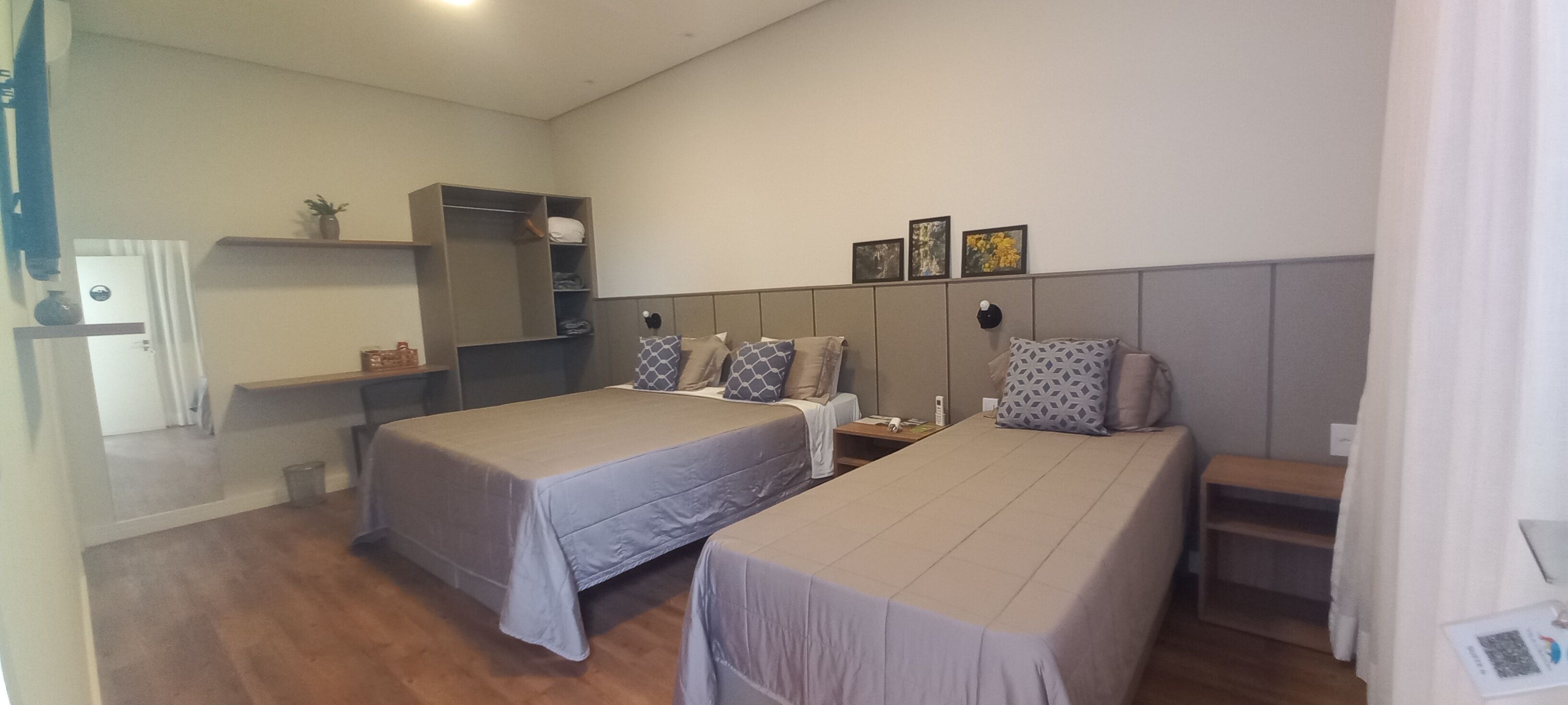 A hotel room with two beds, a wardrobe, a small table, and a shelf with decorative items.