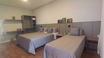 A hotel room with two beds, a wardrobe, a small table, and a shelf with decorative items.