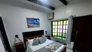 Un dormitorio con cama, mesita de noche, un cuadro, ventana con cortinas y una puerta.