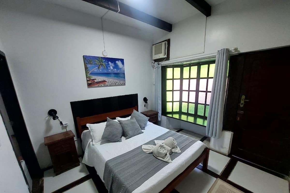 Une chambre à coucher avec un lit, une table de chevet, un tableau, une fenêtre avec des rideaux et une porte.