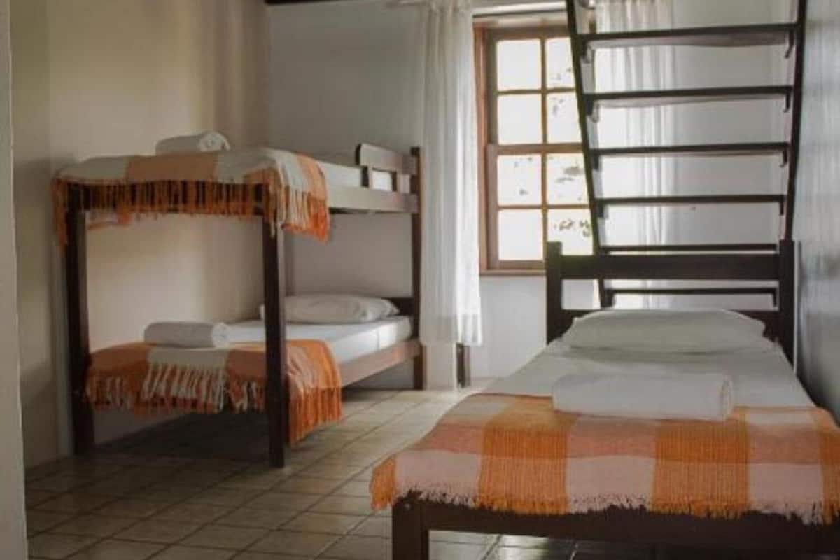 Une chambre avec un lit superposé, un lit simple et une fenêtre avec des rideaux.