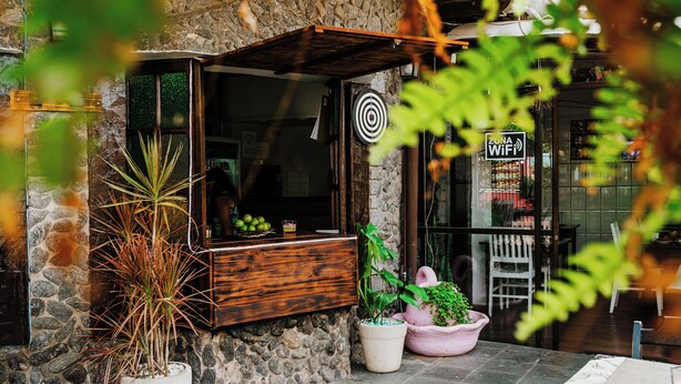 Un área de estar al aire libre rústica, con pared de piedra, banca de madera y plantas en macetas.