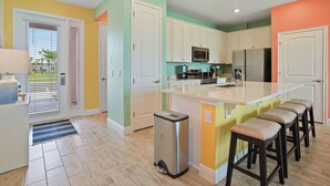 Una cocina moderna con armarios blancos, un refrigerador de acero inoxidable, un microondas y una cafetera.