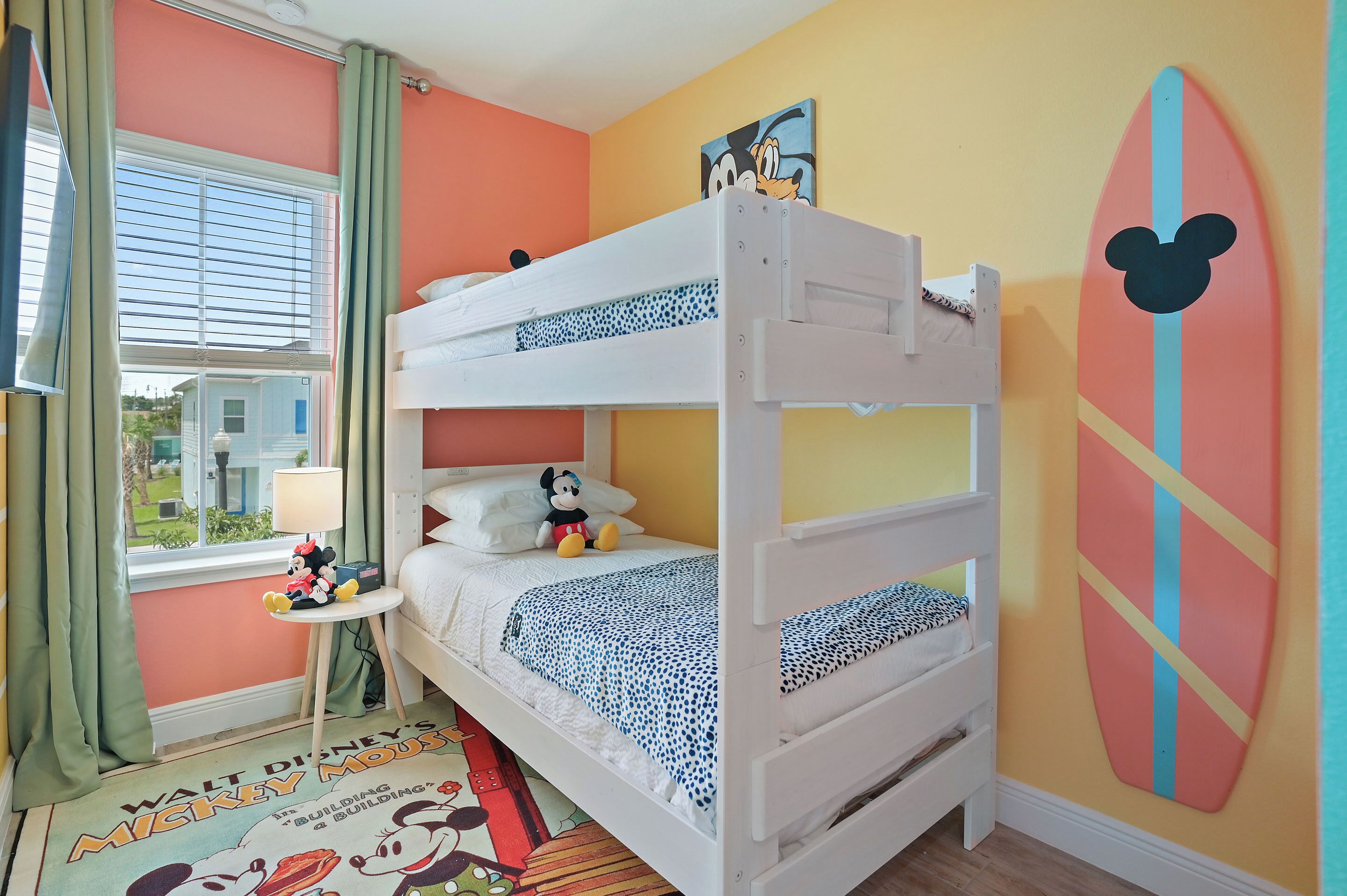 Een slaapkamer met stapelbed, een Mickey Mouse surfplank aan de muur, een Mickey Mouse knuffel op het bed en een Mickey Mouse vloerkleed.