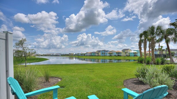 Vista de un lago con una hilera de casas coloridas al fondo, y un área verde con dos sillas Adirondack turquesa en primer plano.