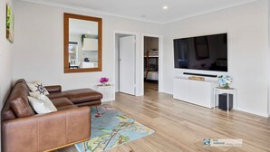 Un salon moderne avec un canapé en cuir marron, un grand miroir, un téléviseur à écran plat et un petit meuble blanc.