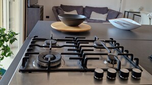 Une cuisine moderne avec une cuisinière à gaz centrale, un saladier posé sur un plateau en bois et un canapé en arrière-plan.