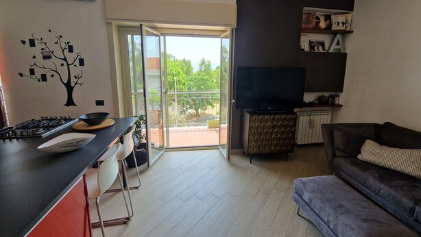 Un salon moderne comprenant un canapé, un téléviseur à écran plat et un coin cuisine avec une cuisinière et une table à manger.
