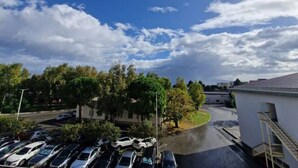 Un parking avec plusieurs voitures, un bâtiment à l’extérieur blanc et un ciel dégagé avec quelques nuages.