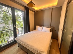 A neatly made bed in a room with a large window, a balcony, and a modern ceiling light fixture. - Hayal Fener (Antalya)