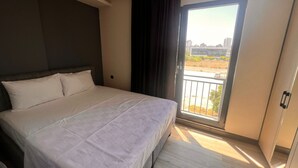 Een moderne hotelkamer met een groot bed, stadszicht vanuit een balkon en een hanglamp.