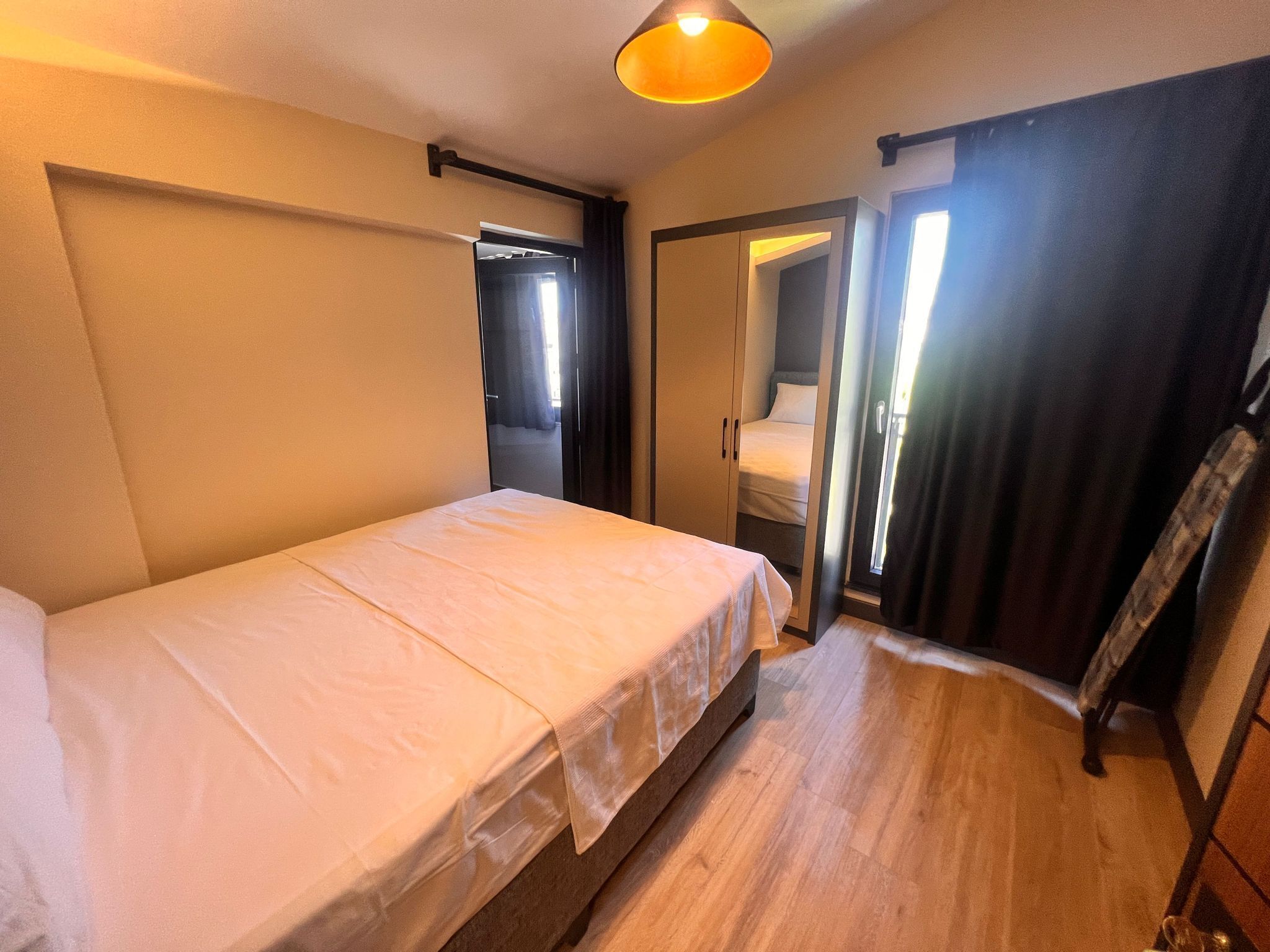 A bedroom with a bed, a wardrobe, a mirror, and a door leading to another room.