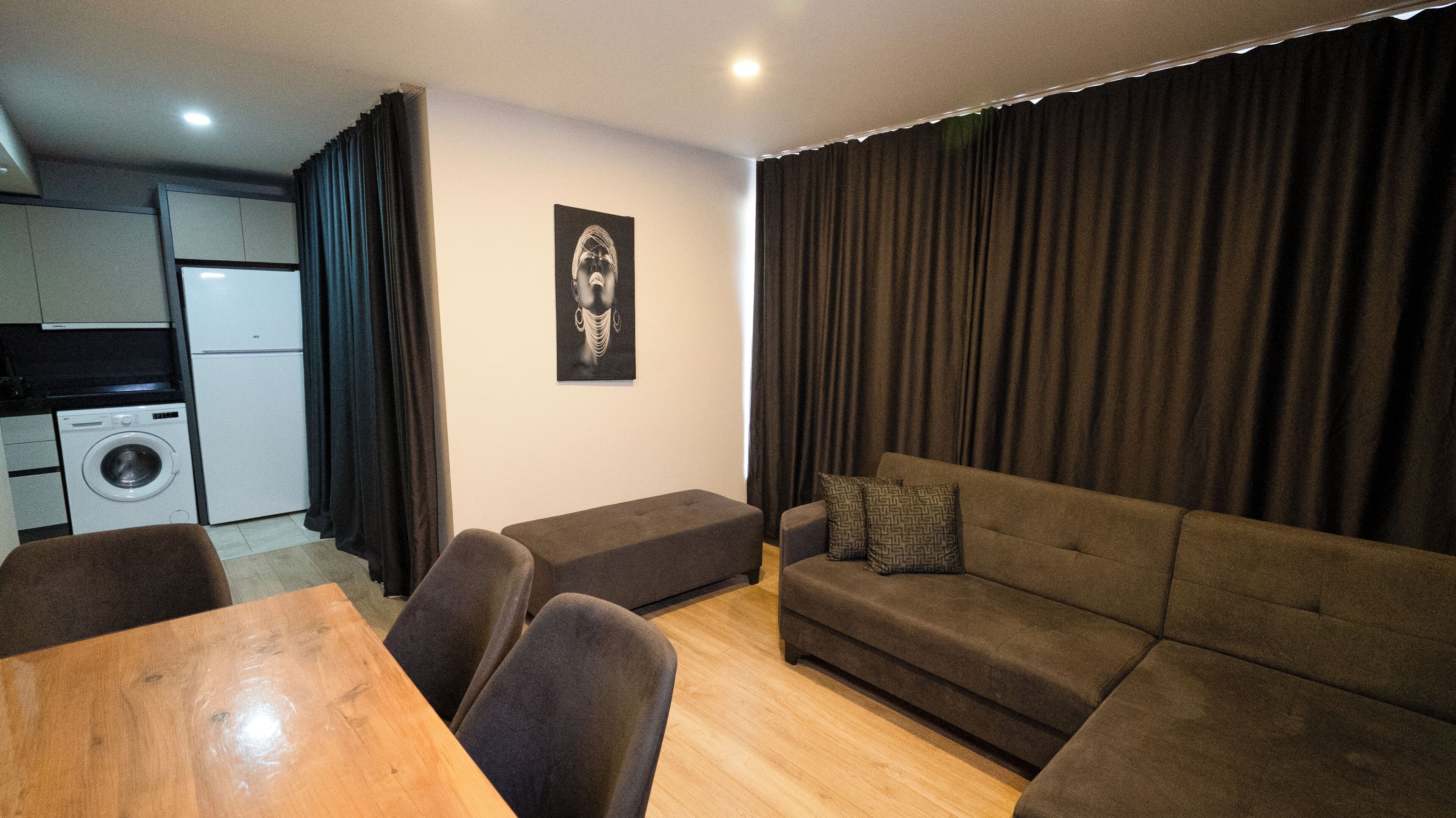 A living room with a sofa, a dining table, and a washing machine in the background.