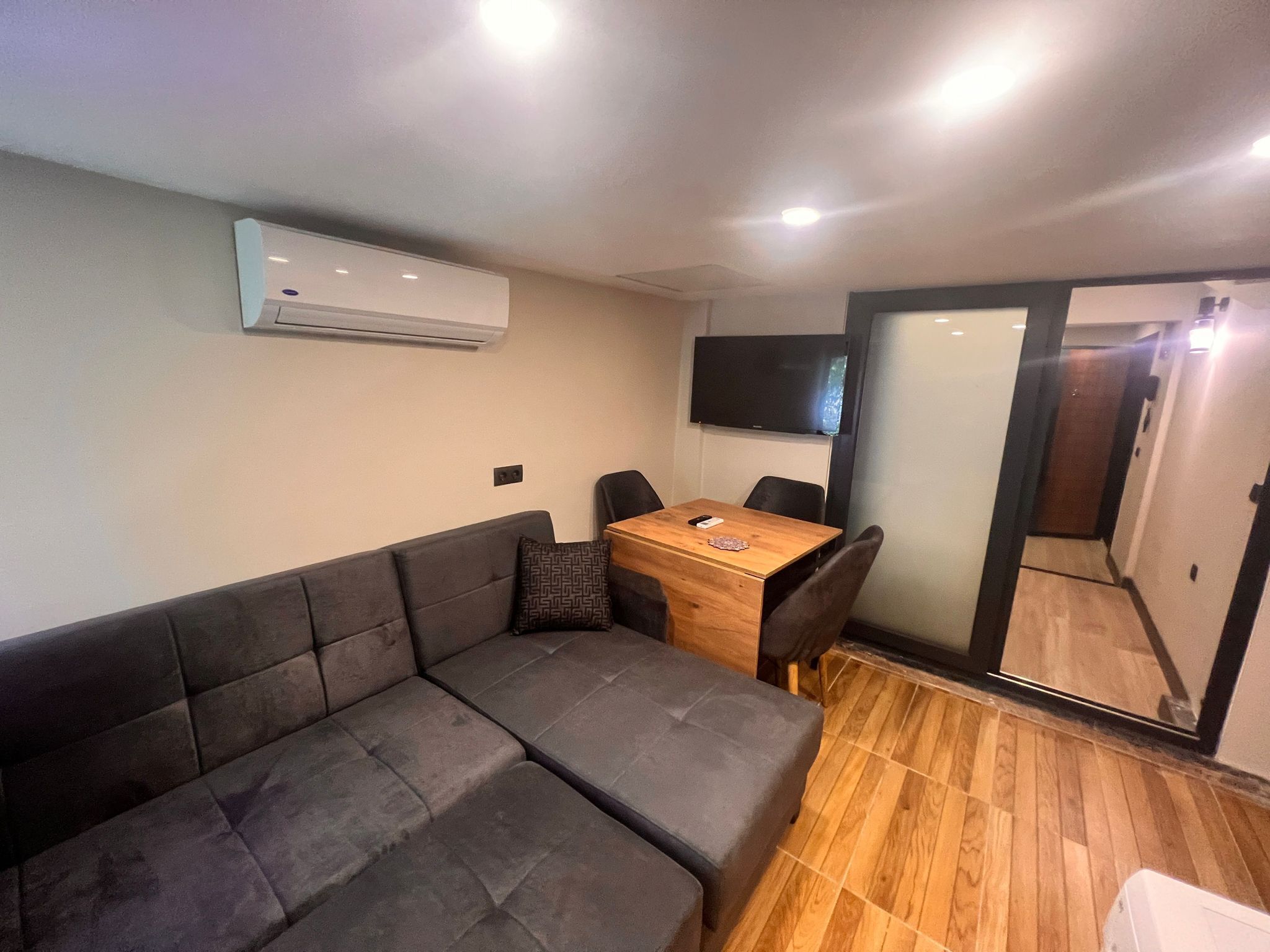 A compact living space with a sofa, a small dining table, and a TV mounted on the wall.