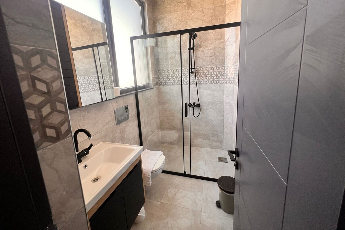 Un baño moderno con ducha de vidrio, lavamanos y retrete.