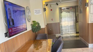 Een moderne vergaderruimte met een houten tafel en grijs gestoffeerde stoelen, een tv met nieuws en een bord waarop staat dat roken verboden is.