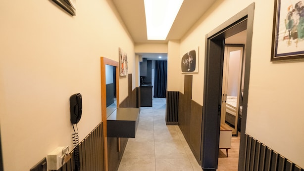 Een hotelgangen met een telefoon, een lijst met kunst, en zicht op een kamer met een bed en een raam.