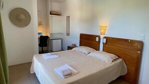 Een net opgemaakt bed met kussens en handdoeken, een klein bureau met een stoel, een lamp en een hoed aan de muur.