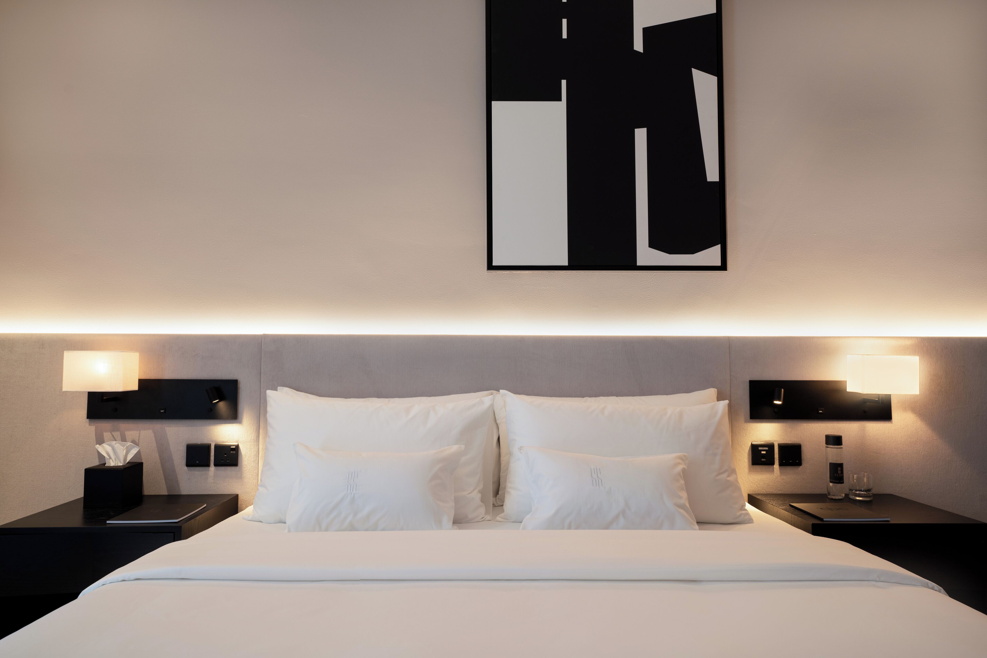 A modern hotel room with a large bed, two bedside tables, and a wall-mounted abstract artwork.