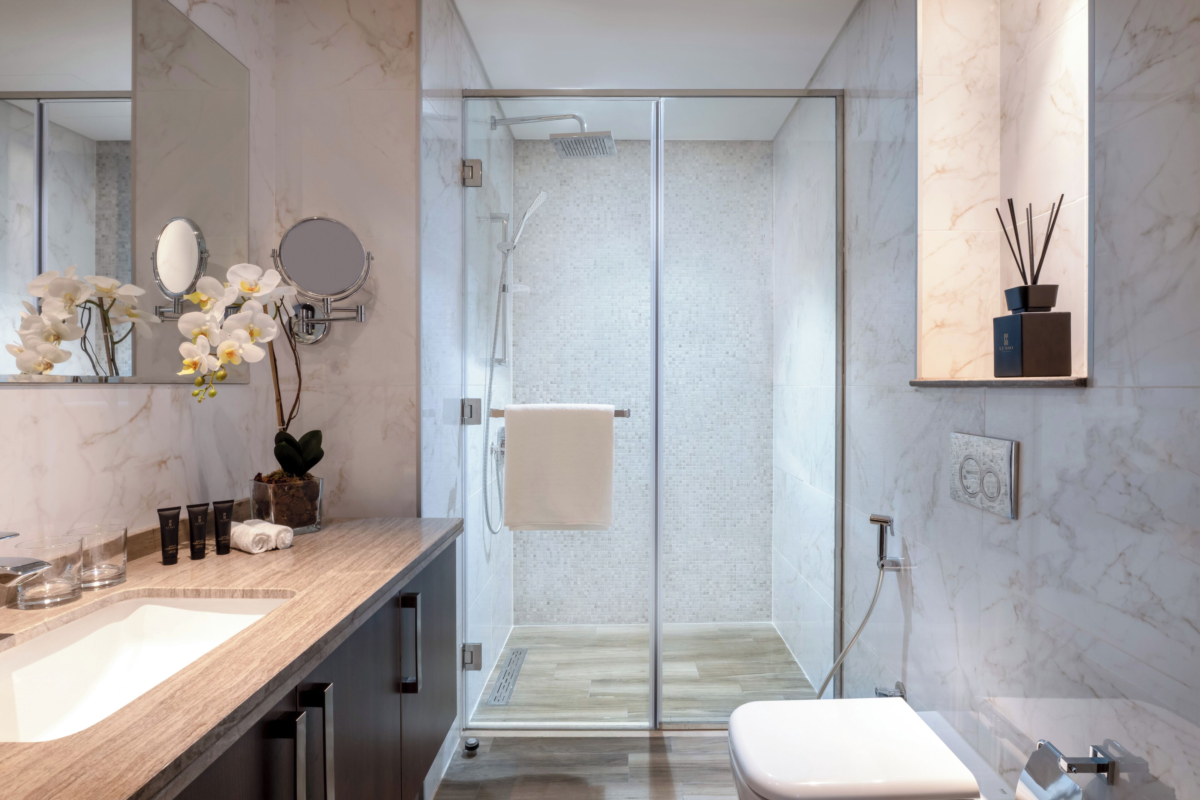 A modern bathroom with a glass-enclosed shower, a large mirror, and a vanity with a sink and toiletries.