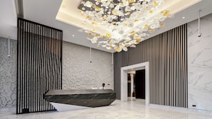 A modern lobby with a marble reception desk, a unique ceiling light fixture, and a patterned wall. - Lusso Hometels J One (Dubai)