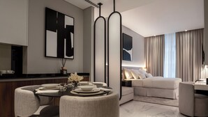 A modern living room with a sofa, a dining area with a table set for two, and a large abstract painting on the wall. - Lusso Hometels J One (Dubai)