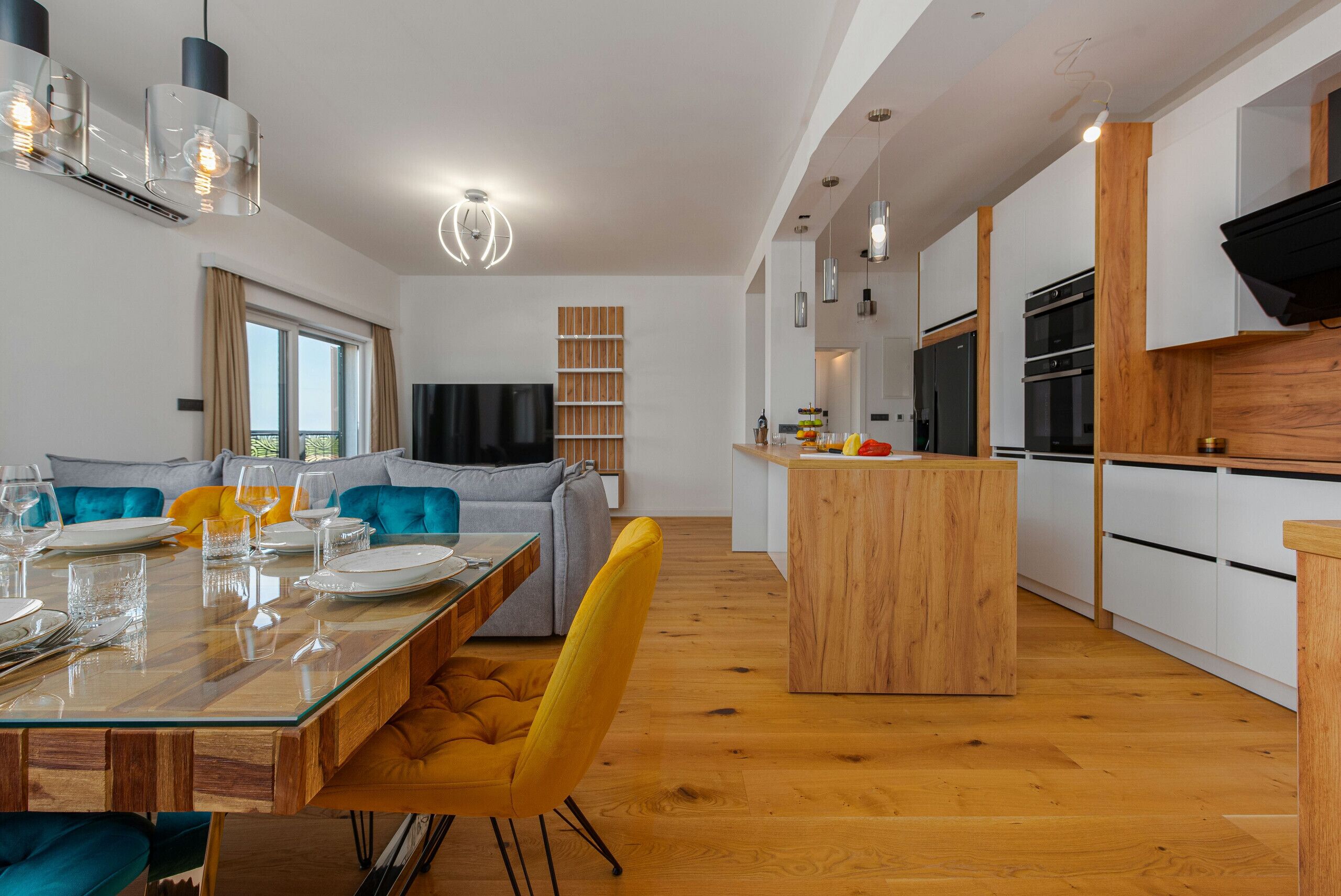 A modern kitchen with white cabinets, a wooden island, and a dining area with a glass table and yellow chairs.