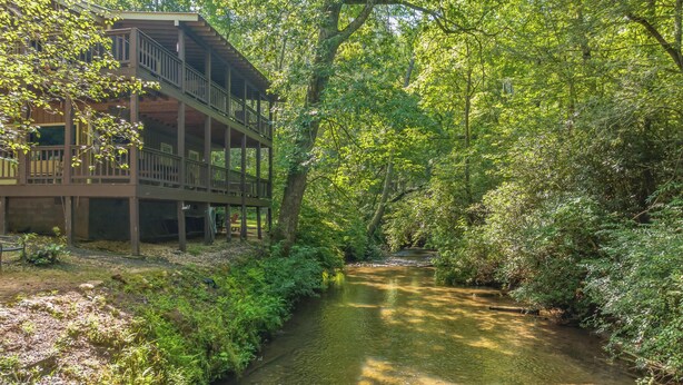 A wooden cabin with a balcony overlooking a clear stream surrounded by dense greenery. - Private retreat at the waters edge of one of NE Ga premier trout streams. (Cleveland)