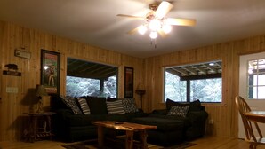 A cozy cabin interior with a wooden floor, a sofa, a coffee table, and a ceiling fan. - Private retreat at the waters edge of one of NE Ga premier trout streams. (Cleveland)