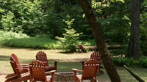 A wooden Adirondack chair set around a small fire pit in a grassy outdoor area with trees in the background. - Private retreat at the waters edge of one of NE Ga premier trout streams. (Cleveland)