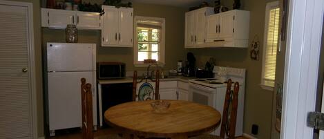 A kitchen with a wooden table and chairs, white cabinets, a refrigerator, a microwave, and a stove.