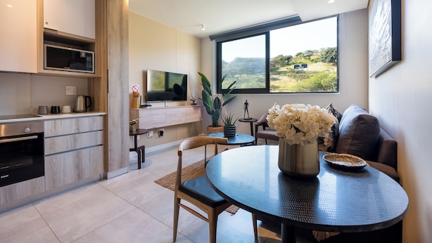 Uma cozinha moderna com forno Bosch, micro-ondas e televisão. Há uma área de refeições com mesa redonda e cadeiras, um vaso com flores e vista para a paisagem através de uma grande janela.