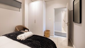 Quarto de hotel moderno com uma cama grande, uma cadeira, um guarda-roupa e uma televisão.