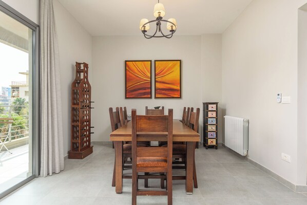A dining room with a wooden table, chairs, a chandelier, and two paintings on the wall.