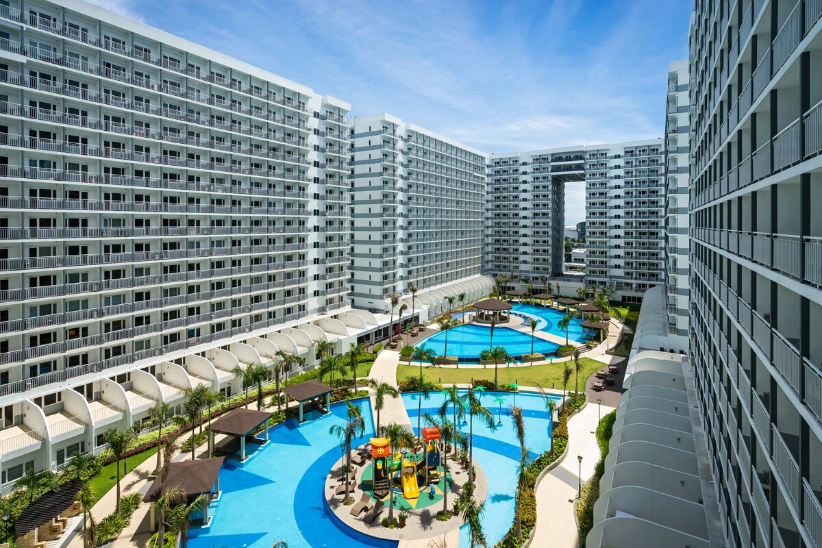 A high-rise hotel with multiple balconies, a central swimming pool, and a children's play area.