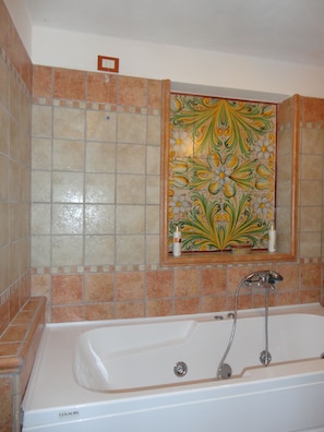 A bathroom with a bathtub, tiled walls, and a decorative tile panel above the sink. - The House of Petra Modica (Modica)