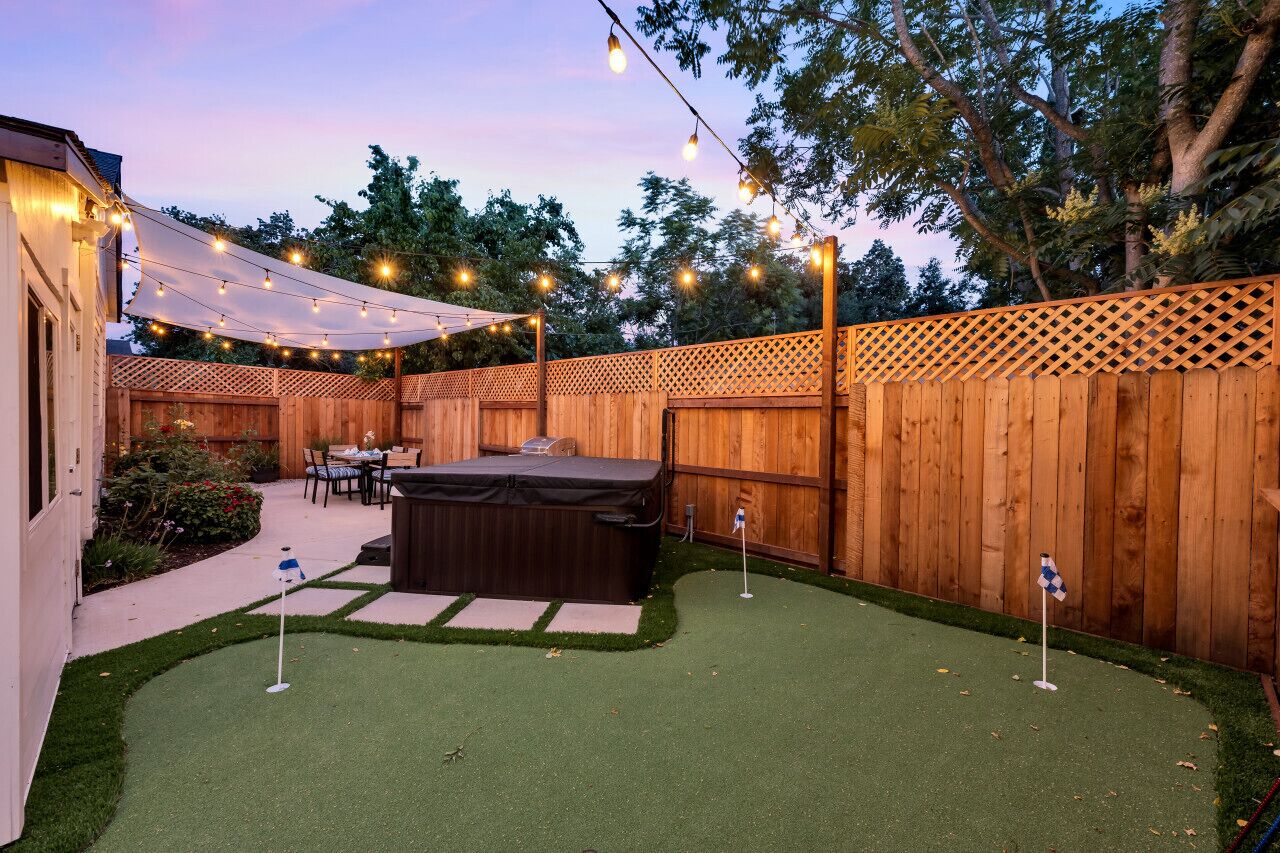 Un jardin avec une pelouse artificielle, un jacuzzi et des guirlandes lumineuses.